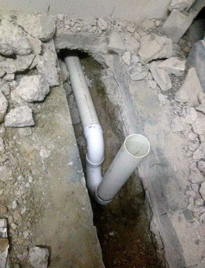 New white PVC drain pipe and fittings laid in a trench cut through a basement concrete floor