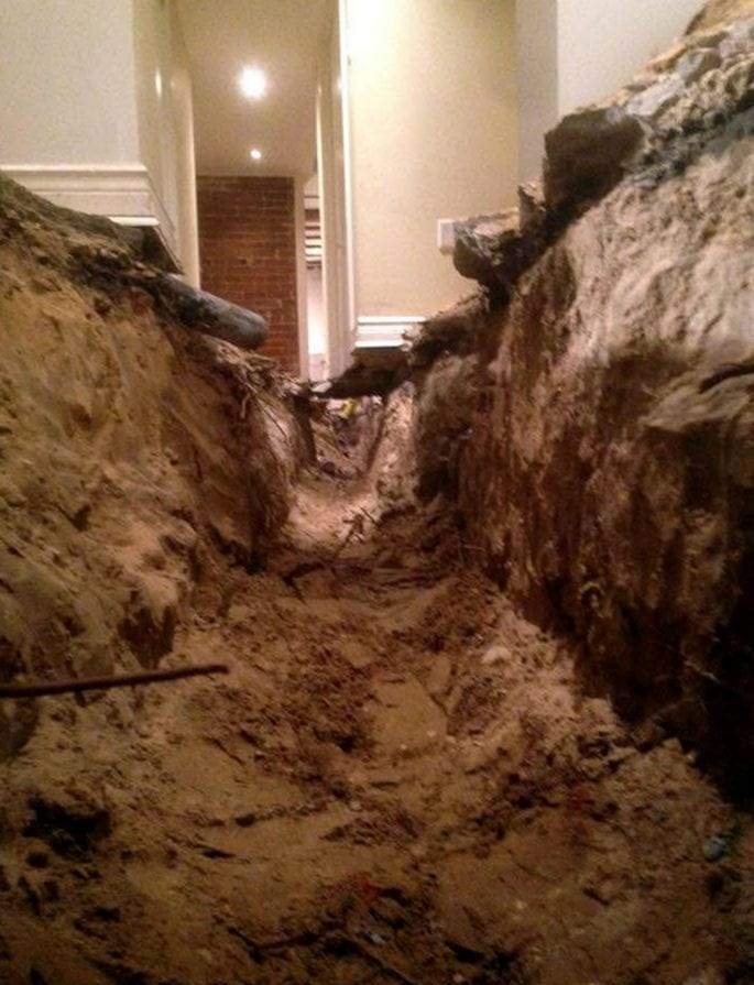 Trench dug through the floor of a finished hallway down to the building sewer pipe