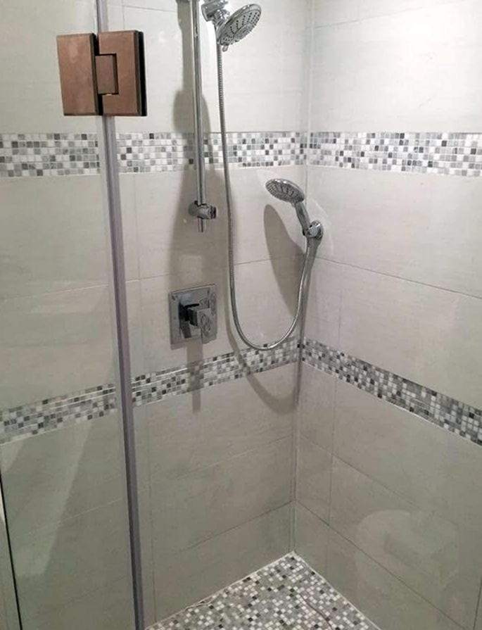 Tiled shower with a slide-bar hand shower, single-handle valve trim and a glass door