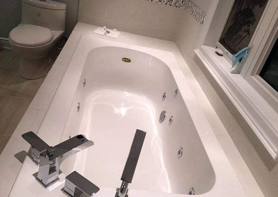 White jetted tub with a deck-mounted chrome faucet and hand shower beside a window