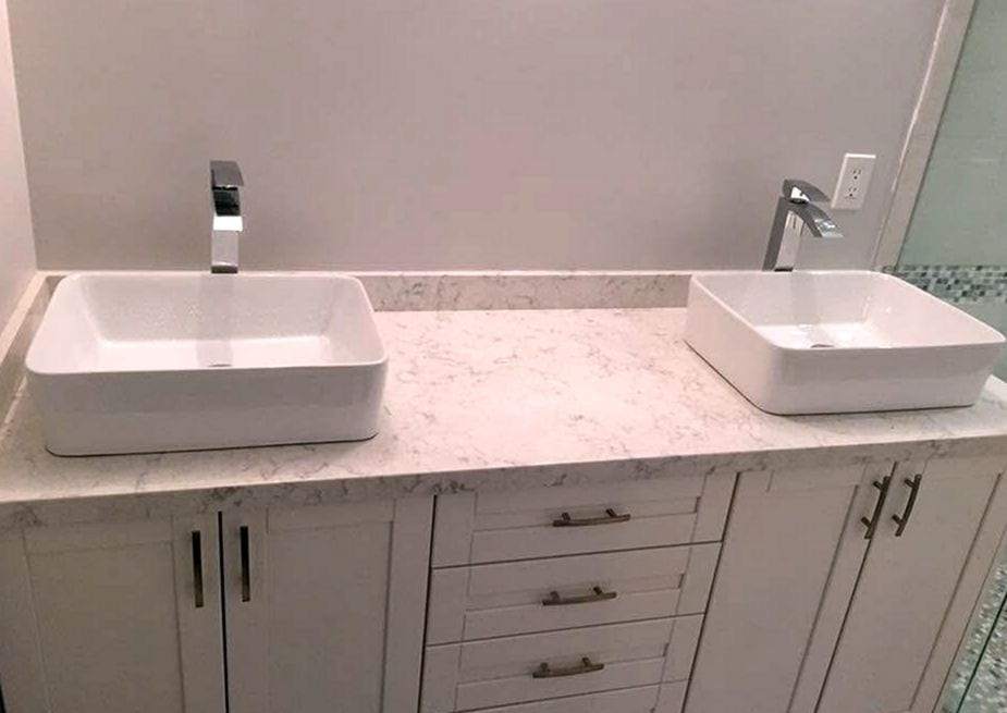 Double vanity with two white vessel sinks, tall chrome faucets and a marble-look top