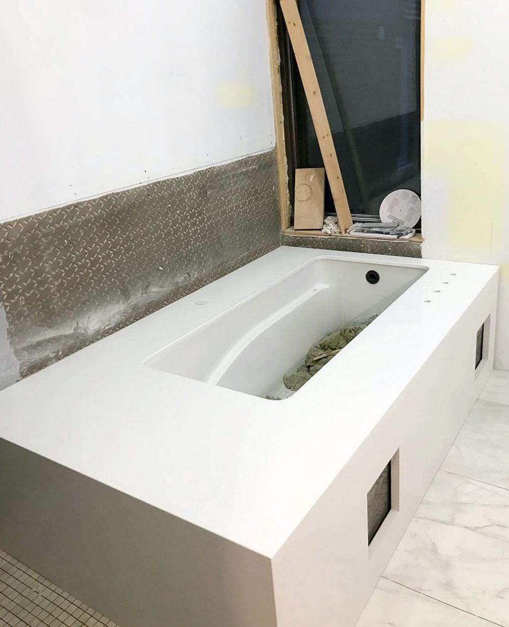 Drop-in bathtub set in a white surround with access panels during a bathroom remodel