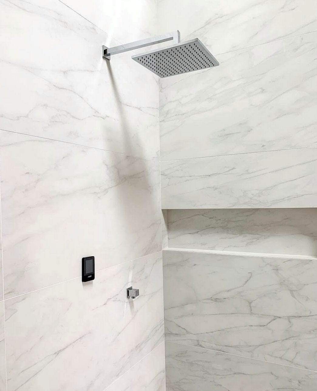 Marble-tiled shower with a square ceiling rain head, a niche shelf and a digital shower control
